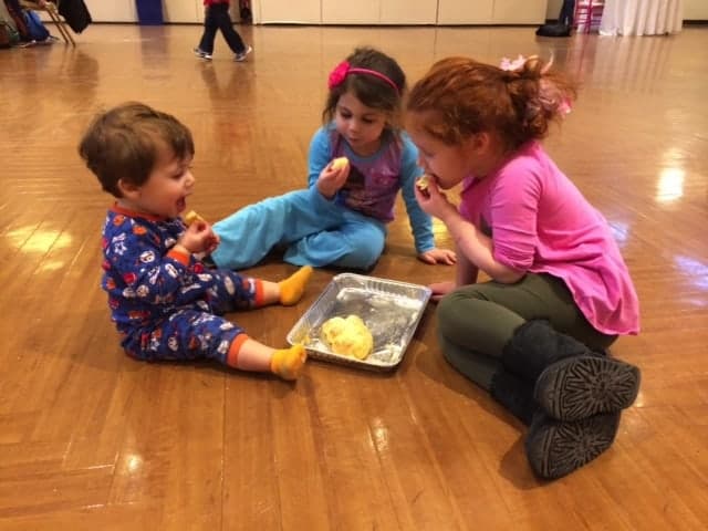 An image of three young children, of slightly different ages, sitting around on the floor and sharing some food. They are happy and getting along together.