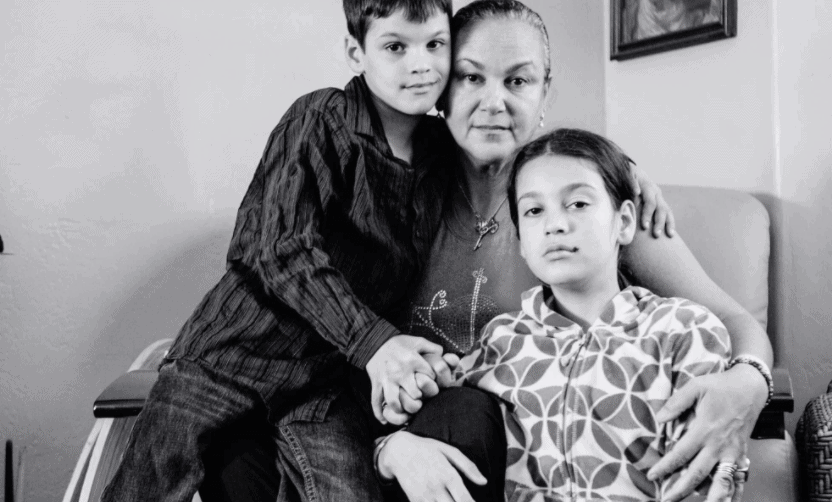 A black and white photo of a family posing together, with a parent and two kids on her lap.